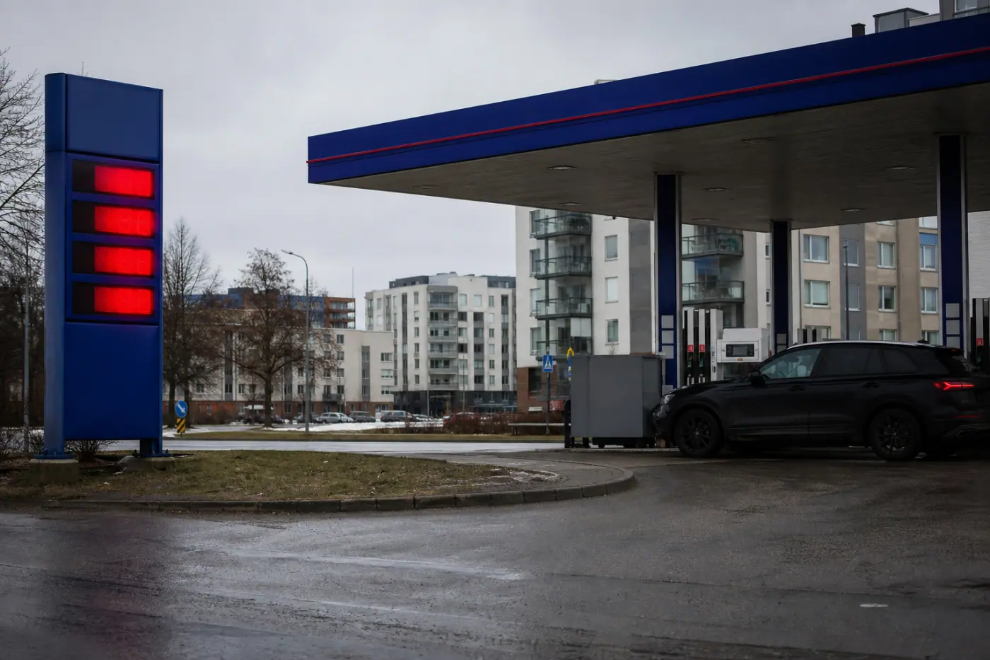 Himmeästi valaistu suomalainen huoltoaseman piha, polttoainepumppu ja auto tankkauspaikalla.