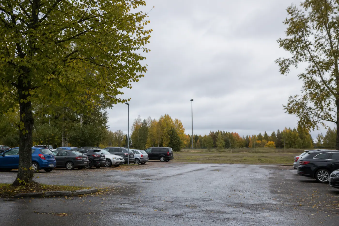 Pysäköintialue Hervannassa, jonka reunalla kasvaa puita ja taustalla näkyy kerrostaloja.