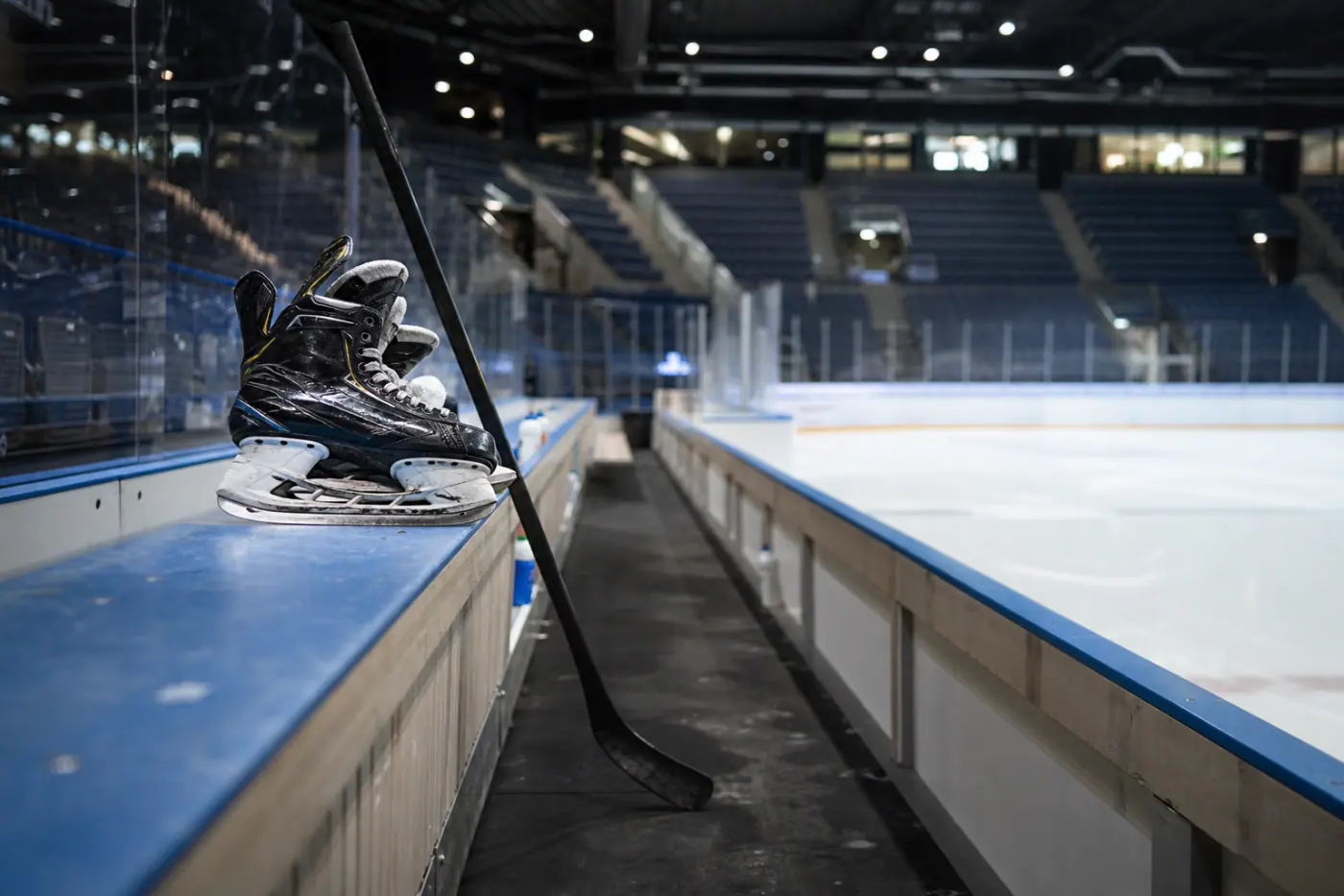 Tyhjä jääkiekkokaukalo, jonka laidalla on luistimet ja maila pelaajien vaihtoaition lähellä.