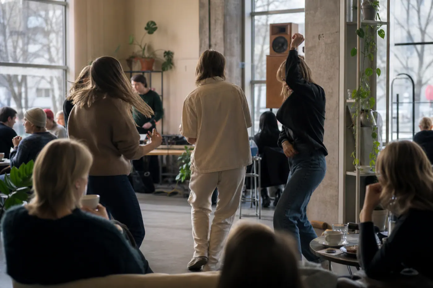 Valoisa kahvila, jossa ihmiset tanssivat pöytien lomassa päiväsaikaan ja taustalla näkyy pieni musiikkilaitteisto.