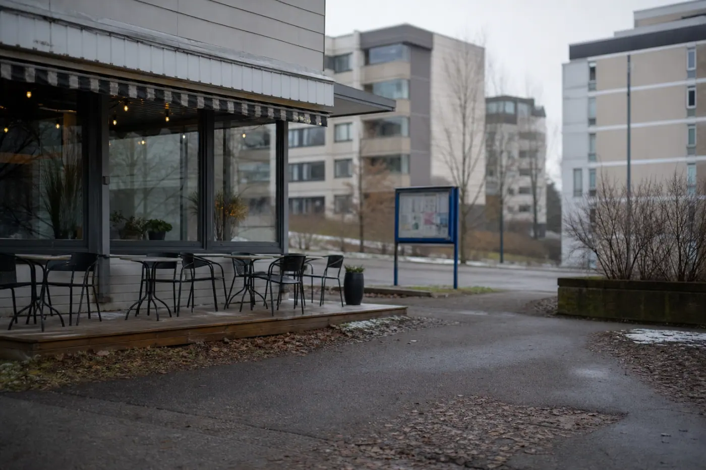 Hervannassa sijaitseva kahvila näkyy ulkoa harmaana päivänä, ja sen edustalla on tyhjiä pöytiä sekä ilmoitustaulu.
