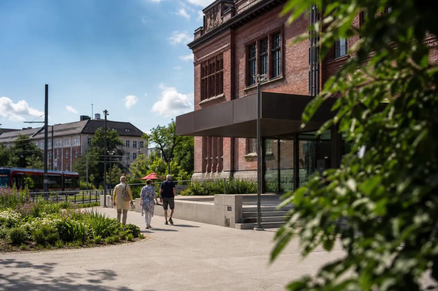Museorakennuksen edustalla on kesäpäivänä muutamia kävijöitä, ja taustalla näkyy tamperelaista kaupunkiympäristöä.