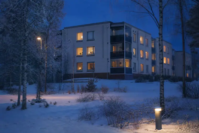 Talvinen Hervannan asuinrakennus iltahämärässä, ja sen valaistuista ikkunoista näkyy pakkasillan lämmin tunnelma.
