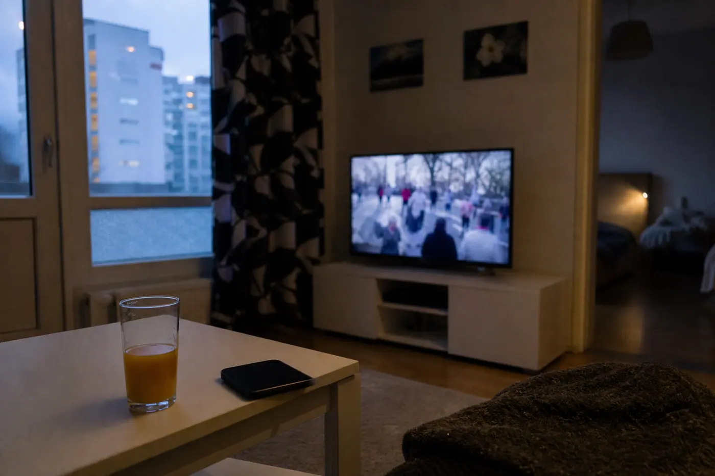 Hervantalaisen asunnon olohuoneessa on televisio, älypuhelin ja lasi mehua pöydällä; televisiossa näkyy epätarkka kansainvälinen uutislähetys.