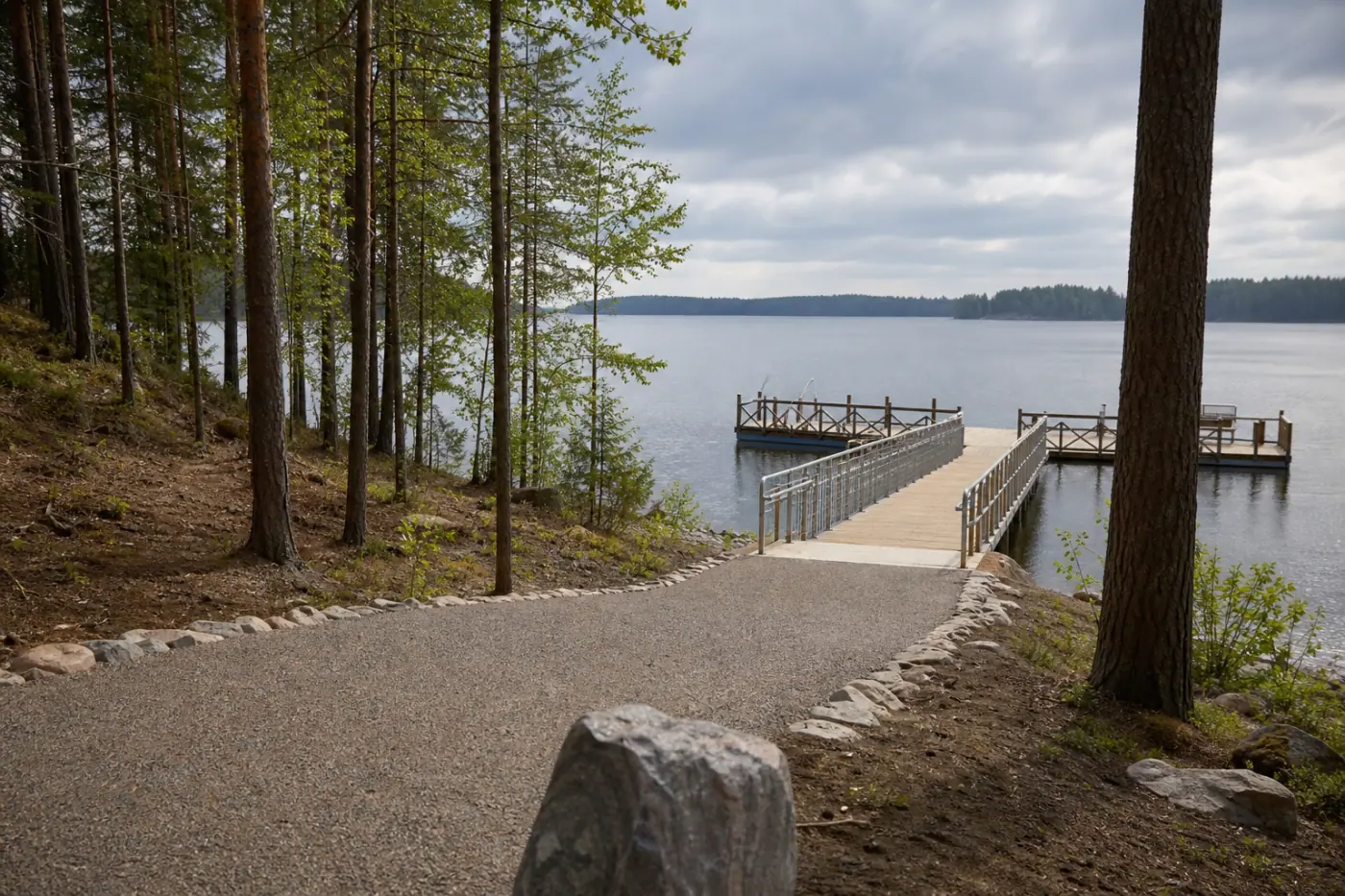 Esteetön kalastuslaituri rauhallisen järven rannalla, laiturille johtava tasainen kulkuväylä ja metsää taustalla.