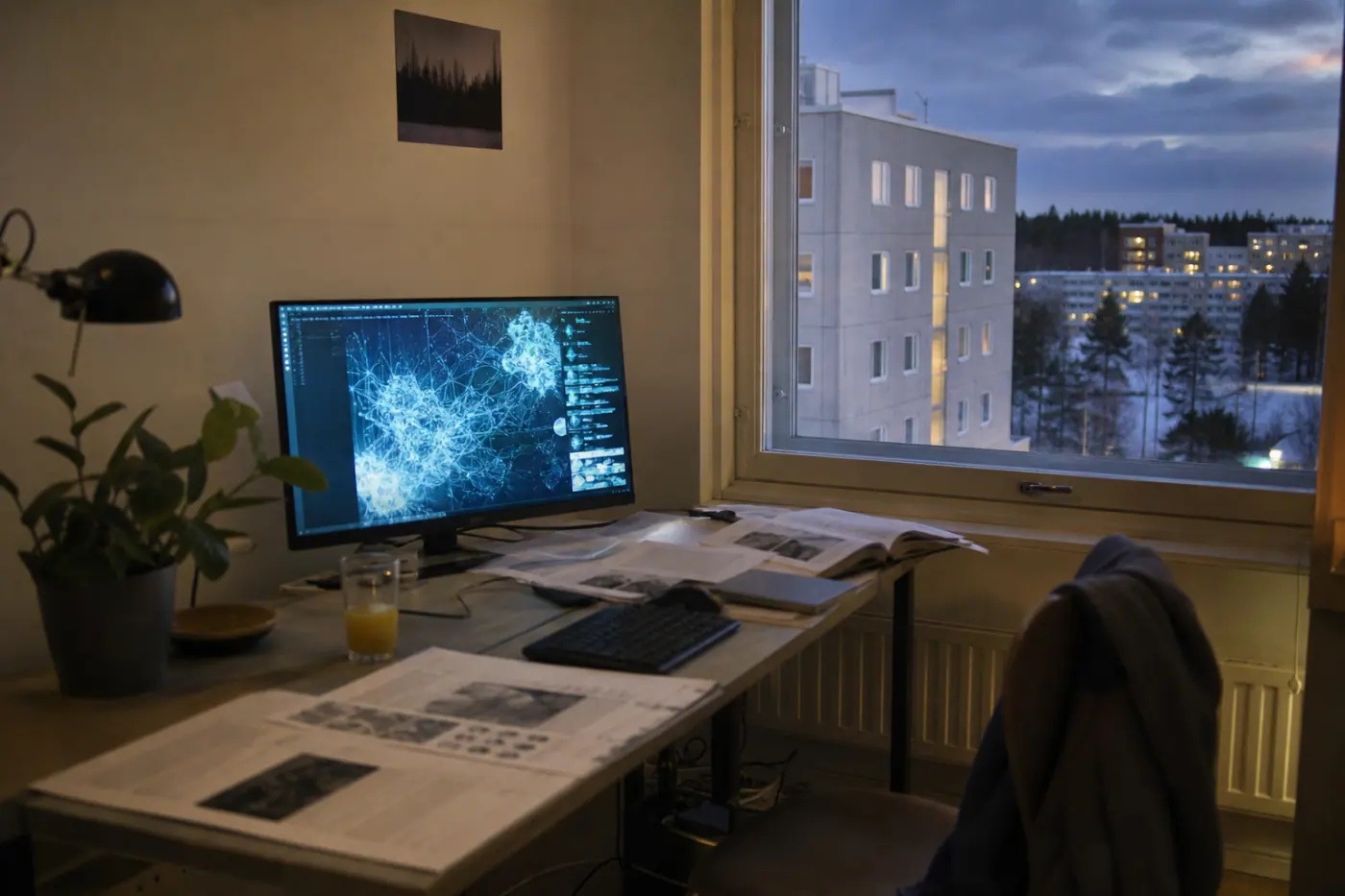 Hervantalaisen asunnon työpöytä, jolla on tietokone, papereita ja lasi mehua hämärässä iltavalossa.