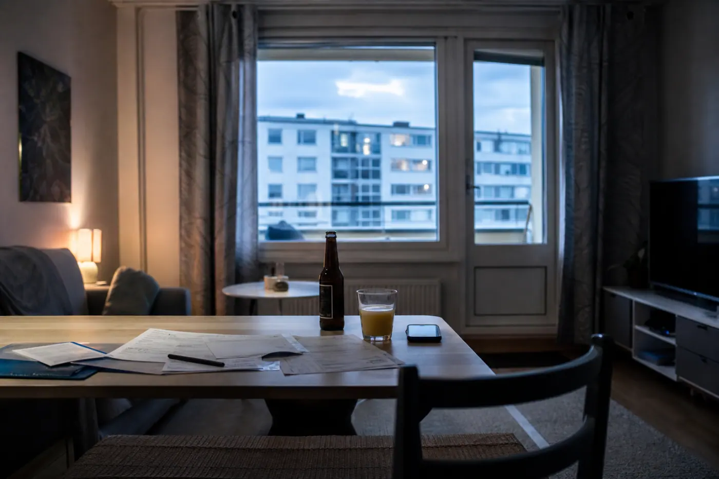 Hervantalaisen asunnon olohuoneen pöydällä on talouspapereita, mehulasillinen ja avaamaton olutpullo.
